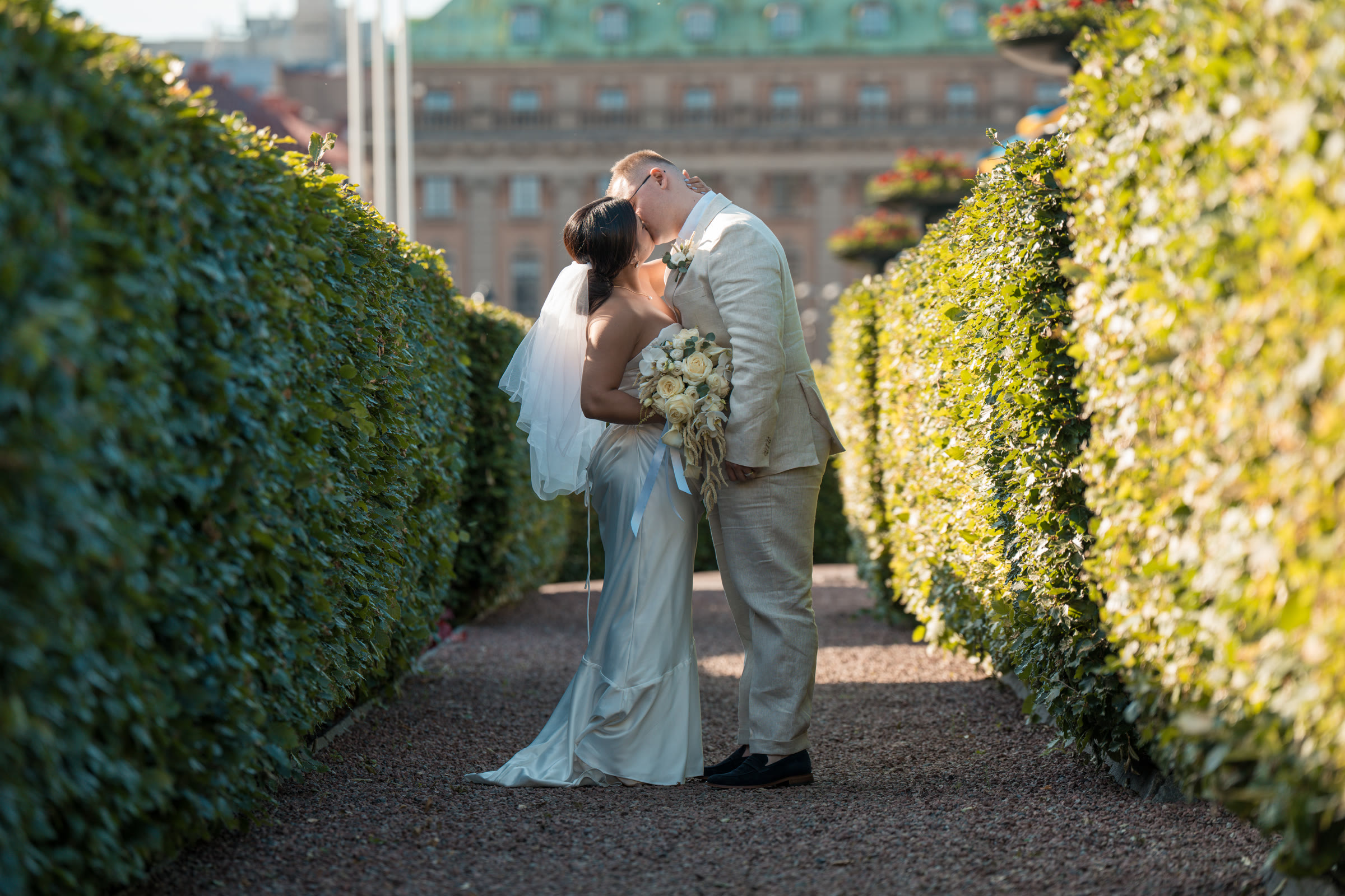 Couple kissing on a hedge-lined garden path